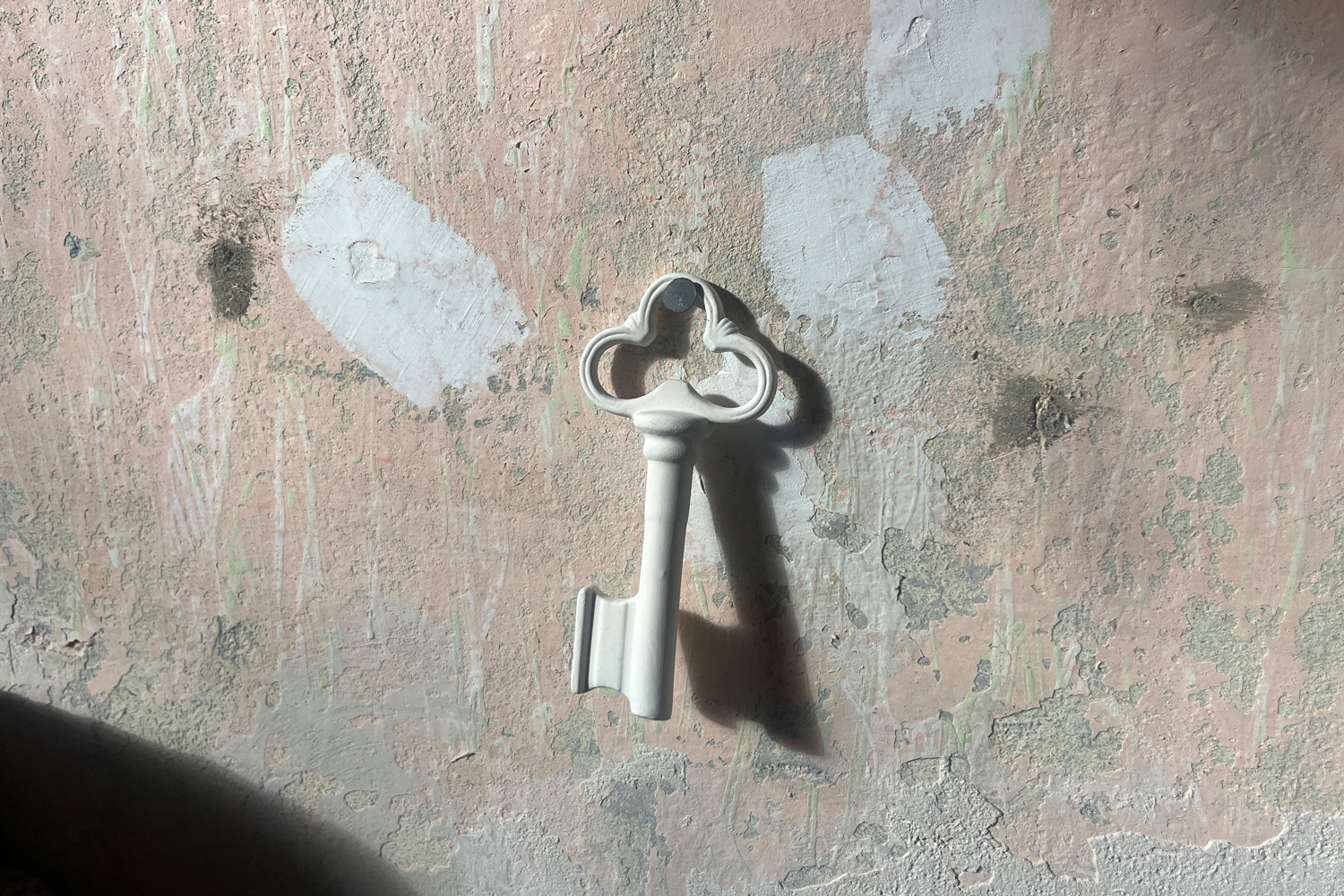 A white porcelain key hangs in the middle of a rough concrete wall.